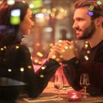 A young couple of a man and a woman dressed in black while holding hands romantically the table romantic restaurant