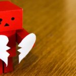 Red square paper robot holding paper broken heart