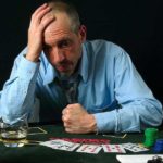 Sad and stressed man in blue shirt gambling and drinking alcohol