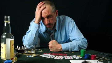 Sad and stressed man in blue shirt gambling and drinking alcohol